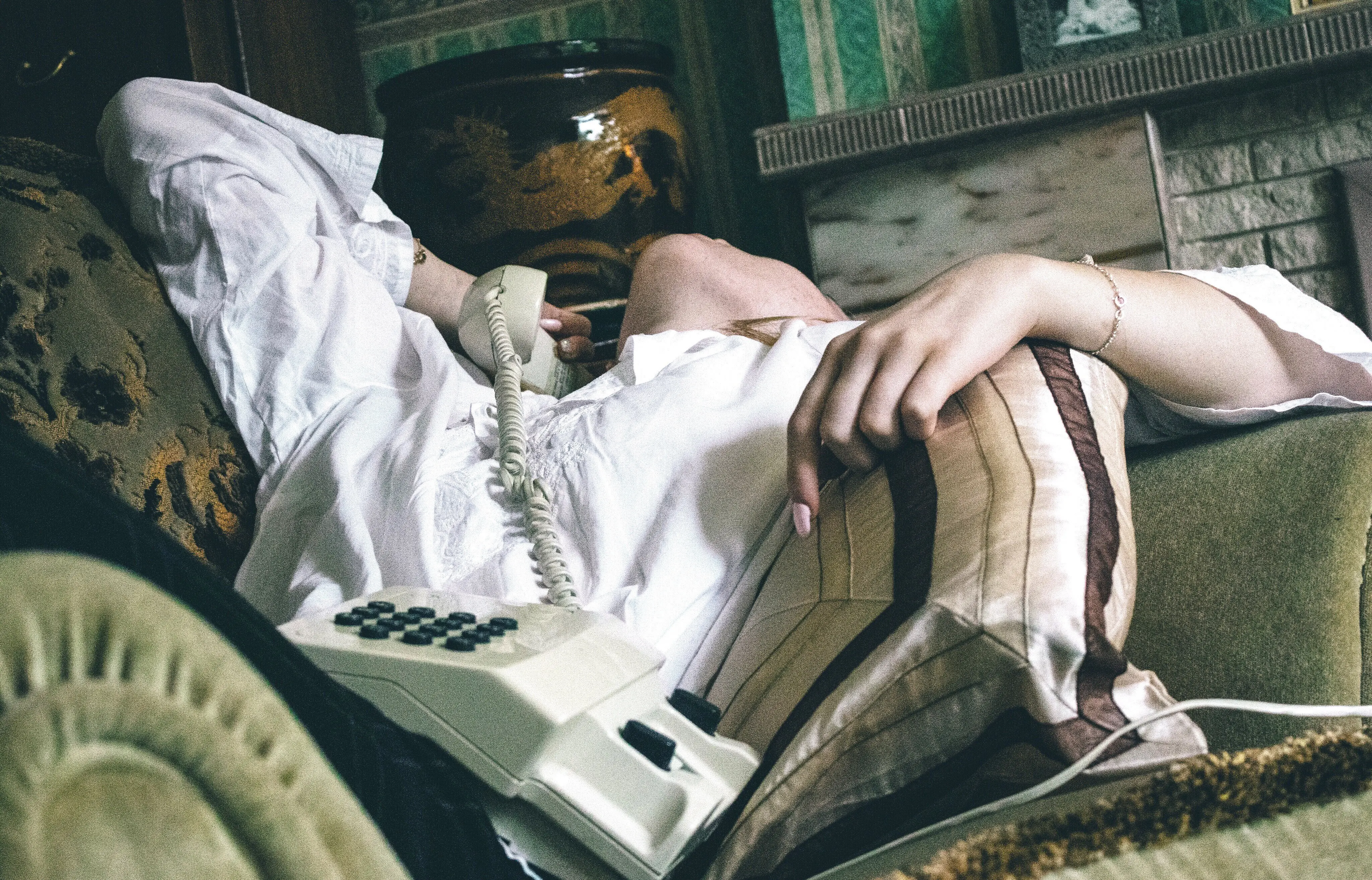 Körpermitte eines Mädchens, das auf dem Sofa liegt und mit einem Festnetztelefon telefoniert.